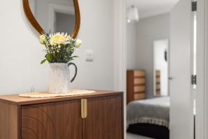 a vase of flowers on a dresser with a mirror at Brand NEW 2 BR Fulham Apartment Near Tube Station COZY in London