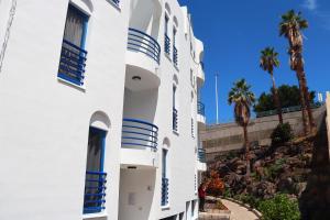 a white building with blue windows and palm trees at BEACHITO Puerto Naos in Puerto Naos