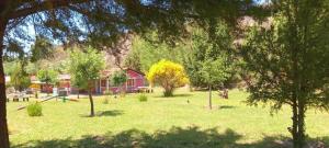a park with trees and a red house in the background at la flor del lugar in Potrerillos