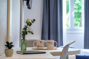 a table with two coffee cups and a vase with flowers at City Résidence Strasbourg Centre in Strasbourg +20 photos