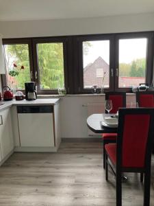 a kitchen with a table and red chairs and windows at Ostfrieslandsuite in Aurich