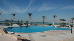 a large swimming pool with palm trees and the ocean at La Hacinda لا سيندا للعائلات in Ras Sedr
