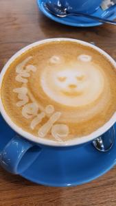 a cup of cappuccino with a face drawn on it at Violetinis namelis/ Sodyba Geras in Anykščiai +4 photos
