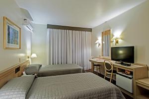 a hotel room with two beds and a desk with a television at Trevi Hotel e Business in Curitiba