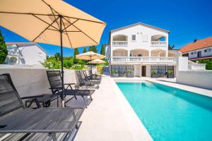 een villa met een zwembad met stoelen en een parasol bij Villa Mia - Moderne Oase mit Meerblick und Pool in Vodice