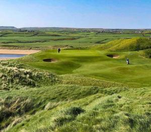 a golf course with two people playing on the green at Cheerful cottage 3-bedroom in Drehidnaraga Bridge