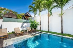 einen Pool mit 2 Stühlen, einem Tisch und Palmen in der Unterkunft Villa Oberoi in Seminyak