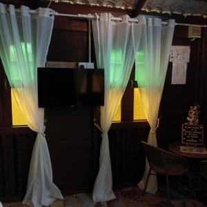 a room with white curtains and a tv and a table at Chinta Chinta Cottage Chalet Kayu in Arau +12 photos