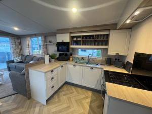 a kitchen with white cabinets and a living room at Fantasy Island - Eastgate F5- The Ardennes with Hot Tub - Coastal Caravan Breaks in Ingoldmells +4 photos