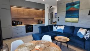a living room with a blue couch and a kitchen at Zakątek Kwiatowa M&K Apartamenty - Gdańsk- Sobieszewo in Gdańsk