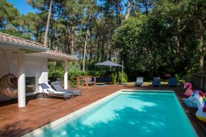 a swimming pool on a wooden deck with chairs and an umbrella at Connemara, Superbe Villa avec piscine, au cœur de la forêt, accès à la plage en vélo in Soorts-Hossegor