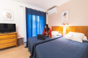 a woman sitting on two beds with a laptop at Les Mimosas - App 07 - Appartement Cosy Clim Balcon 1er étage in Cazaubon