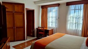 ein Schlafzimmer mit einem Bett, einem Schreibtisch und Fenstern in der Unterkunft Hotel Báez Carrizal in Villahermosa