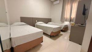 a room with three beds and a television in it at Hotel Jenipapo in Salinas