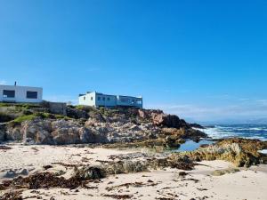 a beach with two houses on a rocky cliff at Thalassa in Bettyʼs Bay