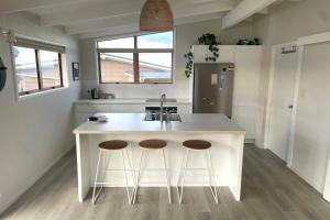 a kitchen with a white island with two bar stools at Tideview Cottage - Incredible Views - Tairua in Tairua