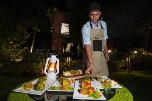 a man standing next to a table with plates of food at Corbett Calling with Projector Set-Up by StayVista in Rāmnagar