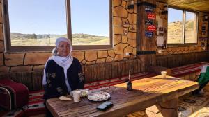 a woman sitting at a wooden table in a room at Dana local life Eco Lodge in Dana