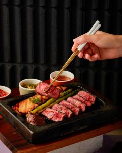 a person is cooking meat on a grill with chopsticks at Sindhorn Midtown Hotel Bangkok, Vignette Collection by IHG in Bangkok