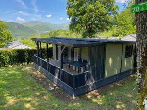 a green tiny house with a porch and a tree at Camping - Piscine - ccbbdag in Vic-sur-Cère