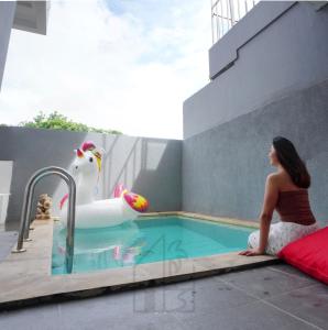 a woman sitting next to a pool with a swan in a swimming pool at Hale lua Villa near Sanur Port in Sanur