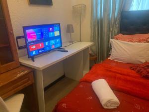 un monitor de ordenador sentado en un escritorio junto a una cama en The Napping Nook, en Ciudad del Cabo