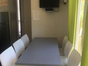 a table with white chairs and a television in a room at Camping le Ranch - Naujac sur Mer in Naujac-sur-Mer