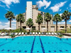 a large pool with chairs and palm trees in front of a hotel at Pullman Sao Paulo Guarulhos Airport in Guarulhos