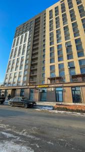 Un gran edificio con un coche aparcado delante. en уютная и стильная студия в новом ЖК Панорама Парк, en Kostanái