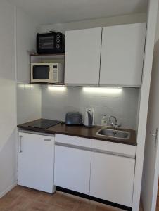a kitchen with white cabinets and a sink and a microwave at Studio cosy Anemone in Luchon