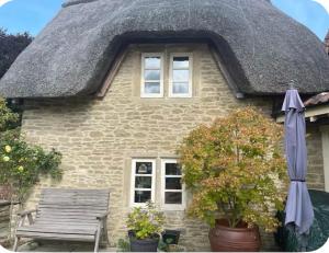 a house with a thatched roof with a bench and an umbrella at Thatch Cottage B&B in Lacock