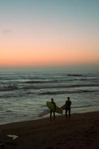 two men walking on the beach with their surfboards at 70's Hostel in Ericeira