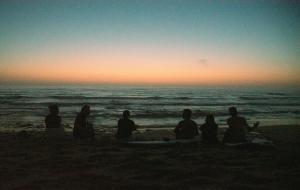 a group of people sitting on the beach watching the sunset at 70's Hostel in Ericeira