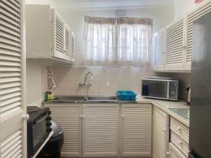 a kitchen with white cabinets and a sink and a microwave at Fishermans Cottage - BillsBest in Port Edward