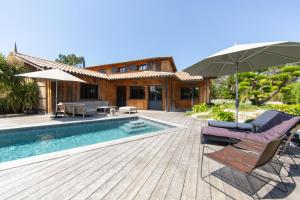 Un patio con piscina y una casa con sombrilla. en VILLA PALOMBES au Cap Ferret, en Cap-Ferret