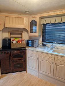 a kitchen with wooden cabinets and a sink and a microwave at Aberystwyth holiday village walking distance to beach, town great outside space parking next to property in Aberystwyth