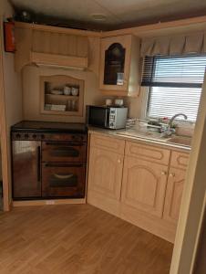 a kitchen with wooden cabinets and a sink and a microwave at Aberystwyth holiday village walking distance to beach, town great outside space parking next to property in Aberystwyth