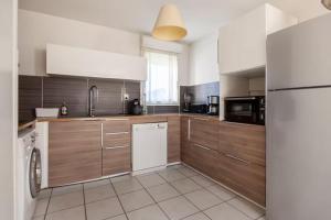 a kitchen with wooden cabinets and a white dishwasher at LE BLEU CAMARGUE - T3 EN DUPLEX CLASSÉ 3 ETOILES - CLIM - ARRIVÉE AUTONOME - Piscine privative à la résidence - Parking Gratuit - Wifi FIBRE - Animaux acceptés - Idéale Famille couple télétravail in Le Grau-du-Roi