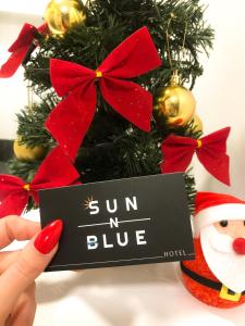 a person holding a sign in front of a christmas tree at Sun N Blue Hotel in Sarandë