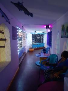 Una habitación con luces violetas y gente sentada en sillas. en Hotel vista mar, en Santa Marta