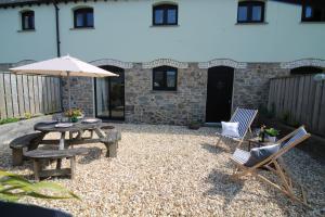 a patio with a table and chairs and an umbrella at The Stable at Widemouth Bay - 2 bedroom cottage both rooms twin or king in Poundstock