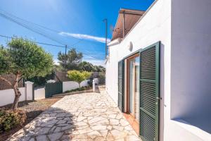 a white house with a green door and a sidewalk at Villa Chiquita in Cala'n Porter