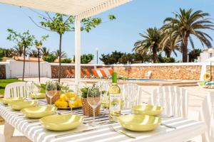 Una mesa blanca con platos blancos y botellas de vino. en Villa Xabec by Villa Plus, en Cala en Blanes