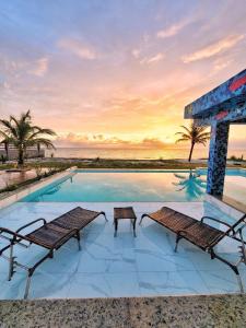 a swimming pool with two benches and the ocean at Pousada Estância Pedacinho do Céu Prado-BA in Prado