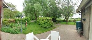a patio with white chairs and a yard with trees at Vakantiehuisje Het Melkmeisje in Kaatsheuvel
