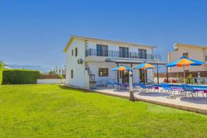 a house with a yard with chairs and umbrellas at Villa Heracles by Villa Plus in Peyia