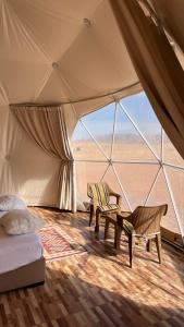 a tent with a bed and two chairs in front of a window at Whispering Rum in Wadi Rum