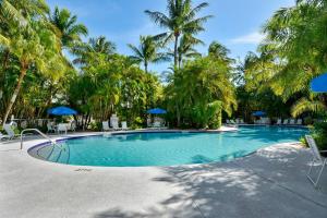 a swimming pool with palm trees and blue umbrellas at Bogeys Retreat by AvantStay Golfers Retreat w Shared Pool Month Long Stays Only in Stock Island