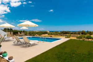 a swimming pool with chairs and umbrellas next to a yard at Orianna Sea View Villa in Gennadi