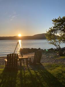 a picnic table and chairs on a beach with the sunset at Kleppa Gard & Glamping in Hjelmeland
